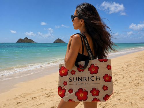 A woman carries the SUNRICH Hibiscus Sun Market Tote on a Hawaiʻi beach with the Mokulua islands behind her